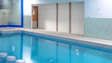 Een binnenzwembad met helderblauw water, betegelde wanden en een betegelde vloer.