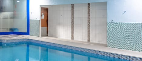 Una piscina interior con agua cristalina, paredes y piso de baldosas.