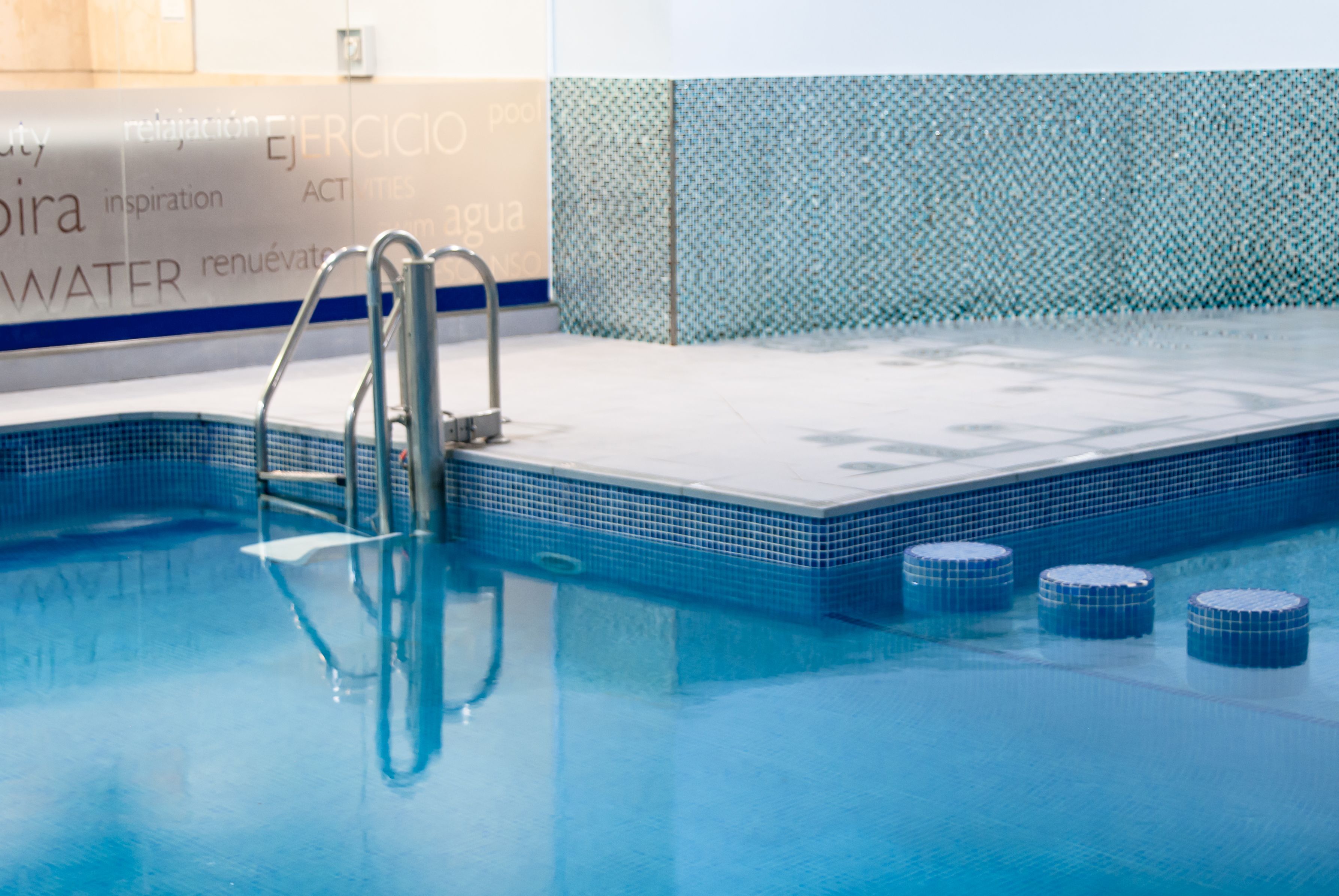 A swimming pool with a tiled edge, a metal ladder, and a tiled wall with text.