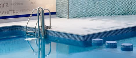 A swimming pool with a tiled edge, a metal ladder, and a tiled wall with text.