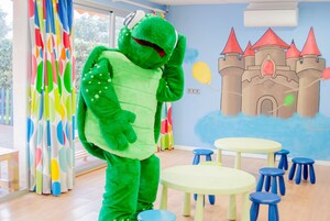 A room with a large green dinosaur mascot, a castle mural, and multiple small round tables and stools.