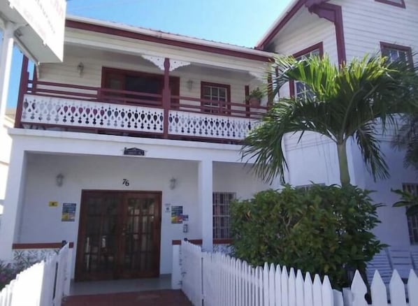 A two-story building with a white facade, a balcony with a decorative railing, and a palm tree in the foreground. - Coningsby Inn (Belize City)