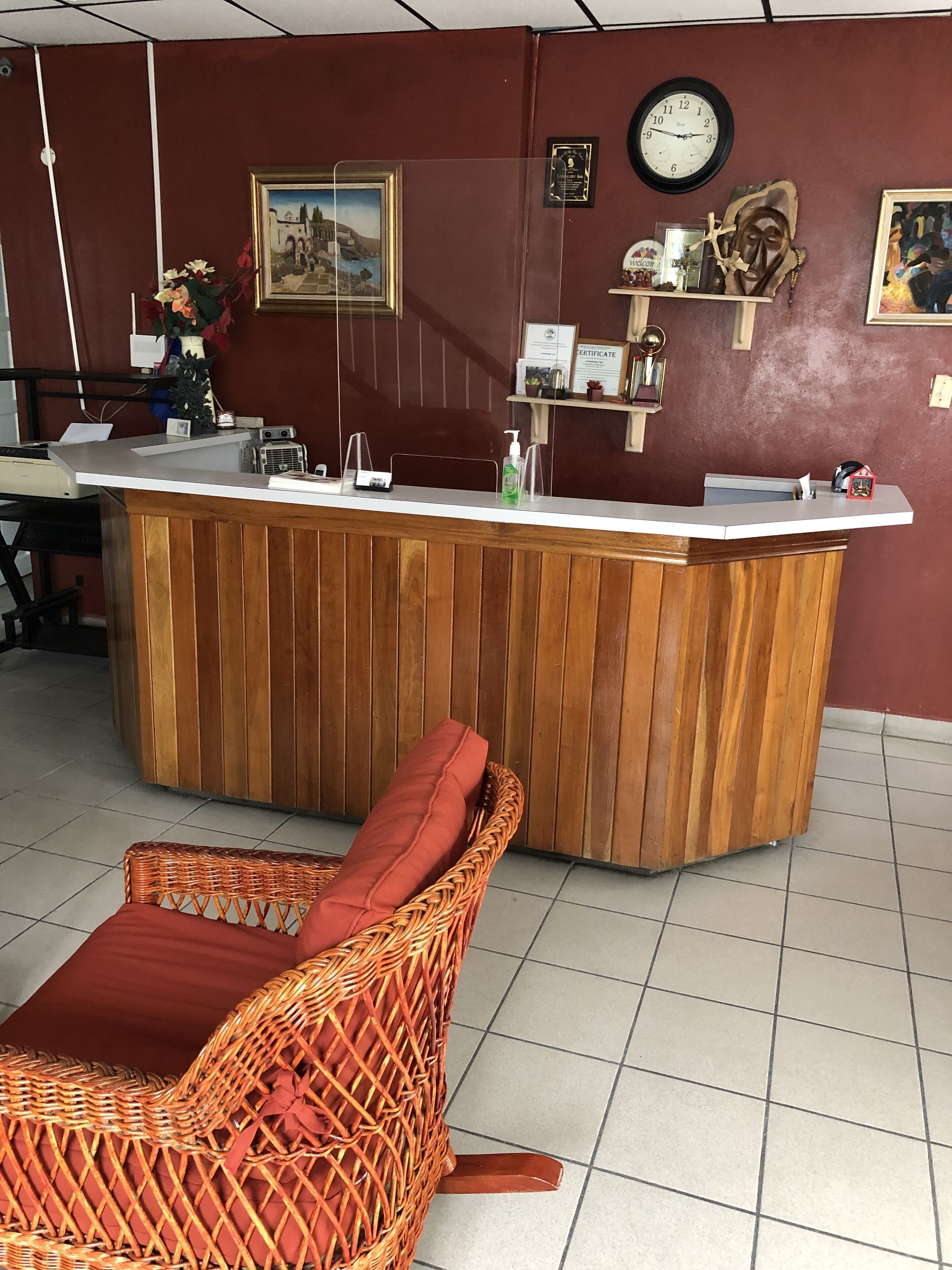 A reception area with a wooden counter, a wicker chair with a red cushion, a clock, and various wall decorations.