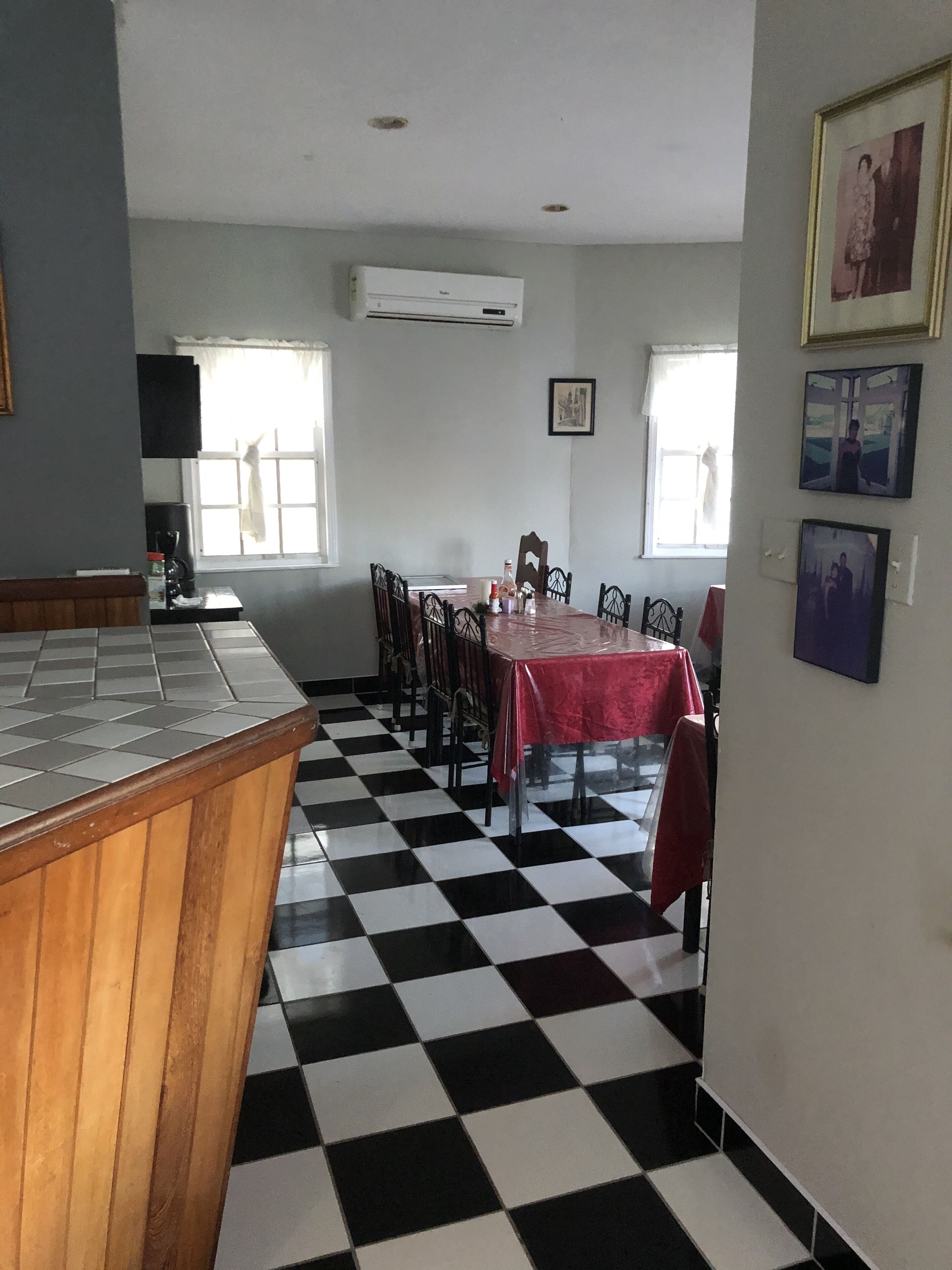 Un coin repas avec un sol à carreaux, une table recouverte d’une nappe rouge et des chaises.