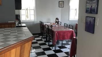 A dining area with a checkered floor, a table with a red tablecloth, and chairs.