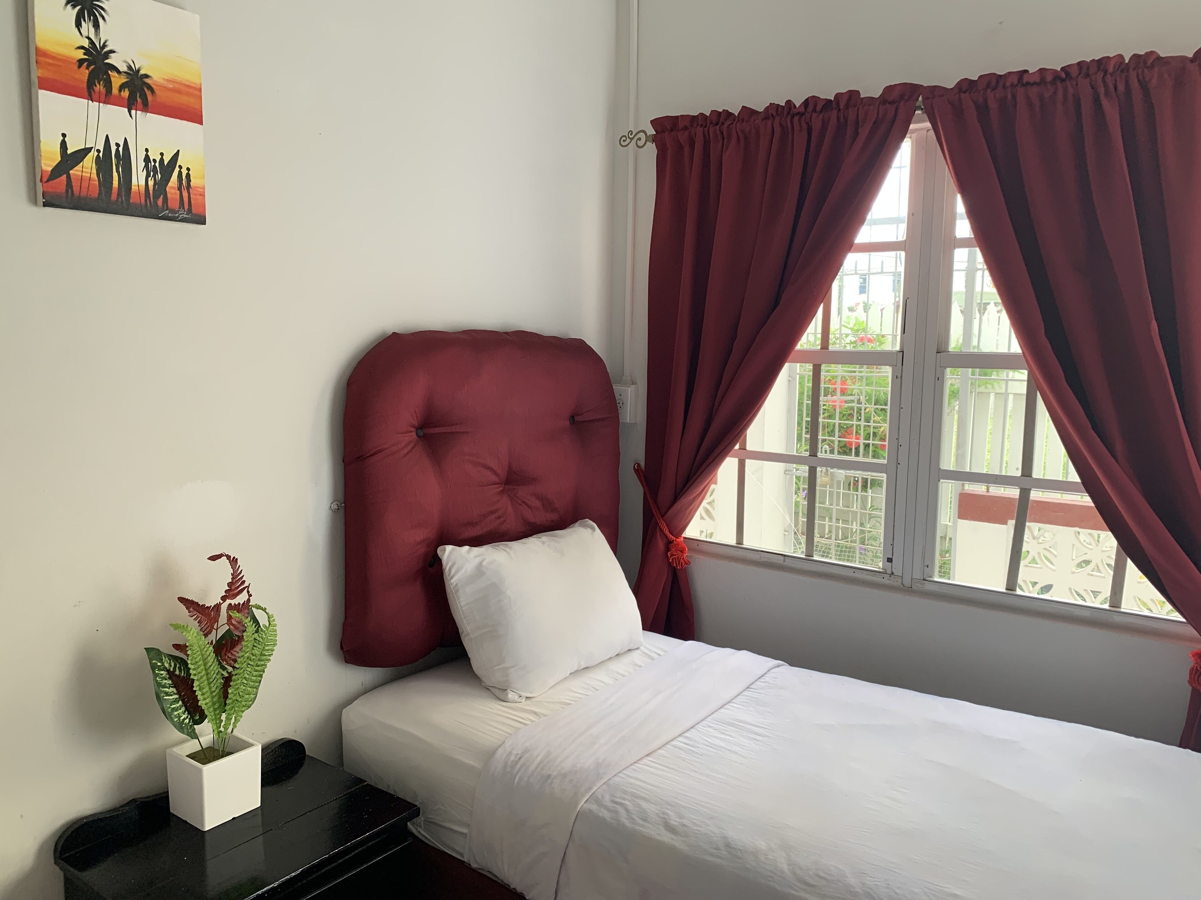 Une chambre à coucher avec un lit, une table de chevet, une plante en pot et une fenêtre avec des rideaux.