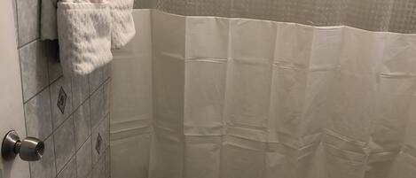 Un baño con un inodoro, una cortina de ducha y dos toallas colgadas en la pared.