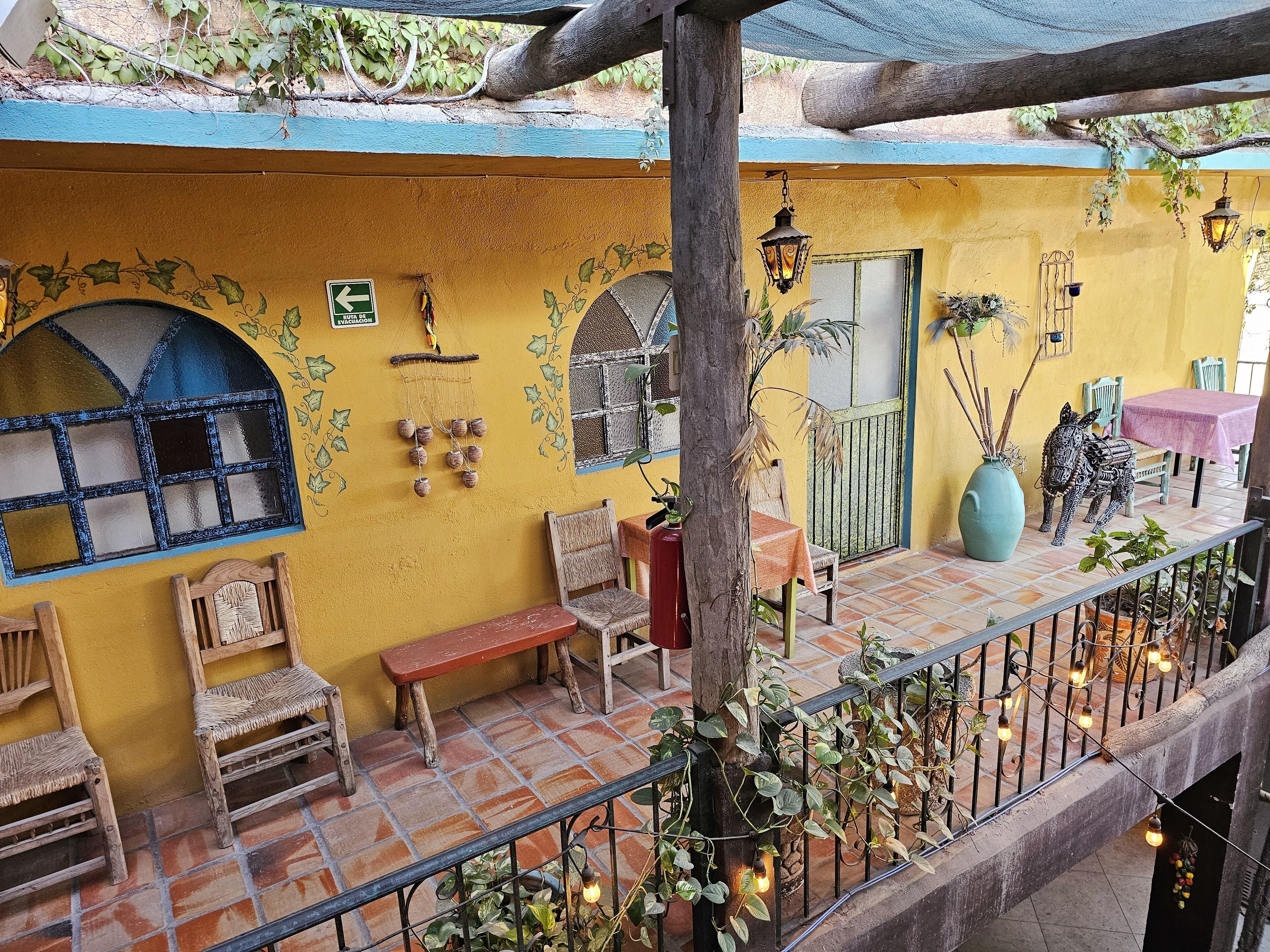 A yellow building with a balcony, wooden chairs, a bench, and a table with a pink tablecloth.