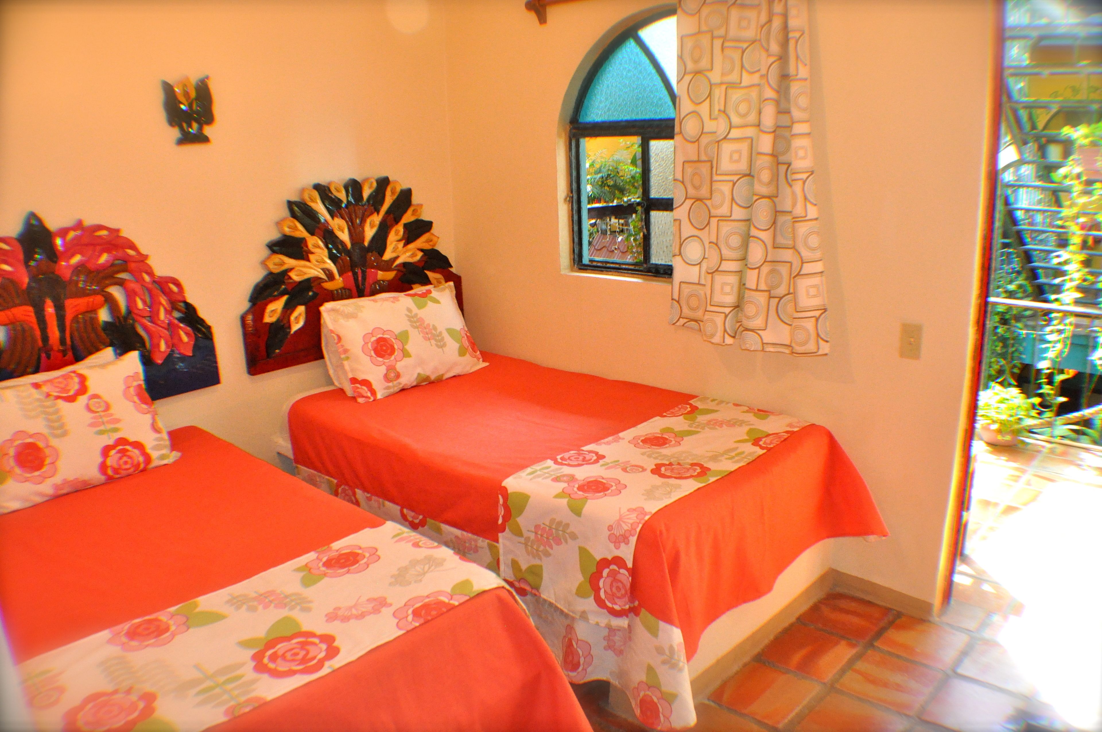 Habitación con dos camas, cada una con colcha y almohadas a juego. Se ve follaje por la ventana.