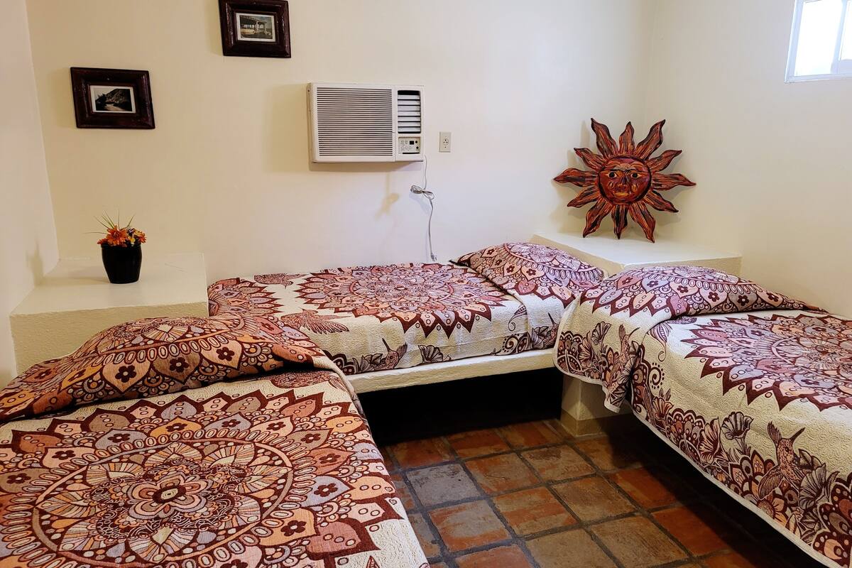 A room with two beds, a wall-mounted air conditioner, a potted plant, and a sun decoration.