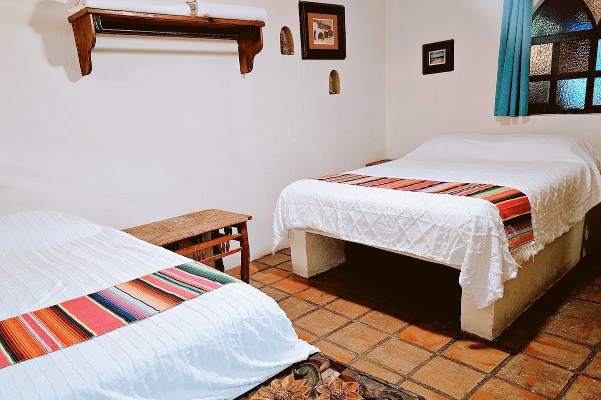 A room with two beds, a small wooden stool, and a decorative table.