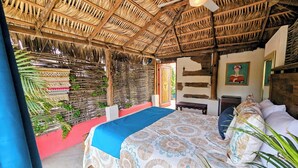 A room with a thatched roof, a bed with a patterned bedspread, a ceiling fan, and a wall with a mural. - Cabo Inn Hotel (Cabo San Lucas)
