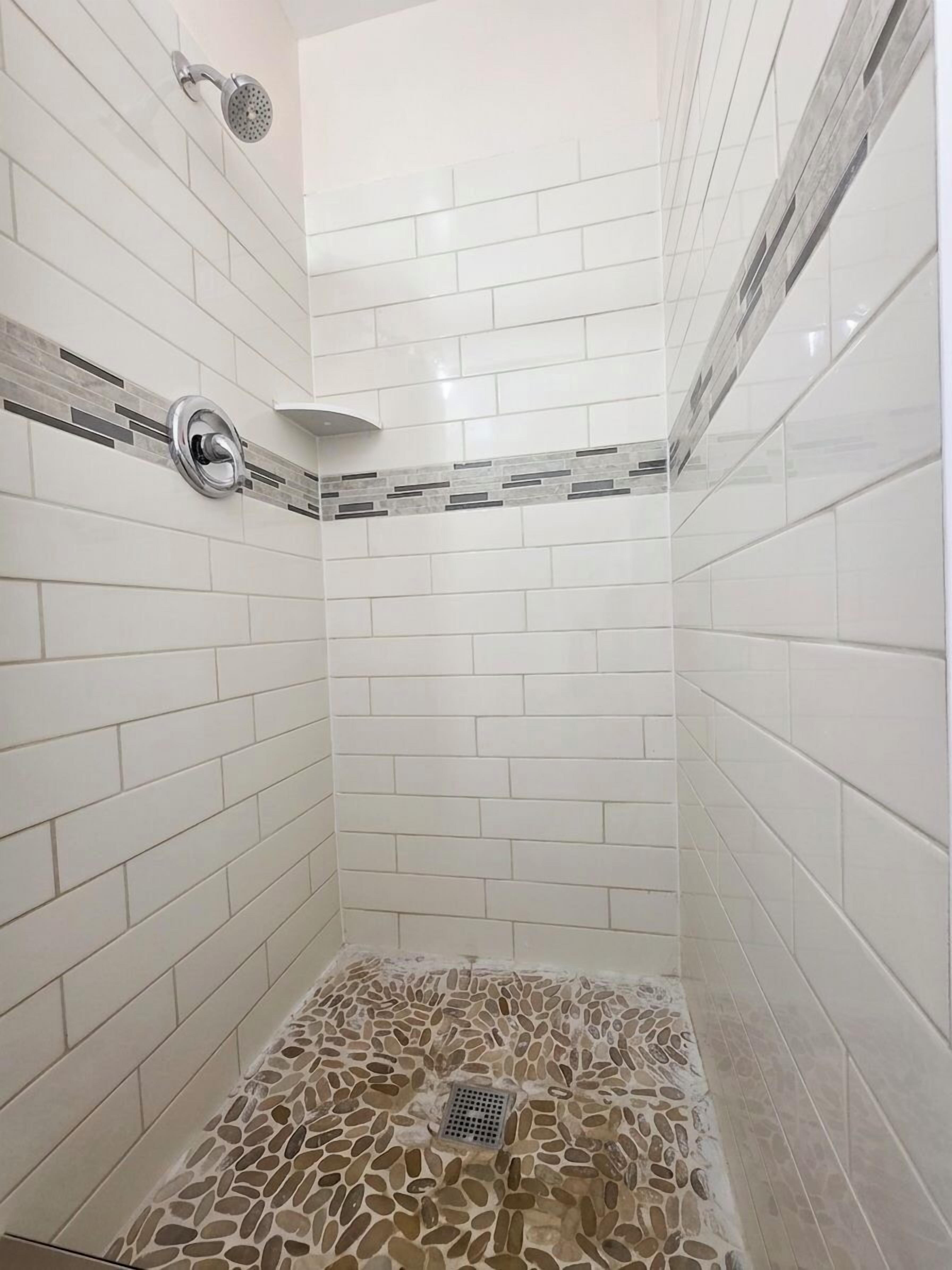 Una ducha con azulejos blancos y suelo de mosaico de piedra.