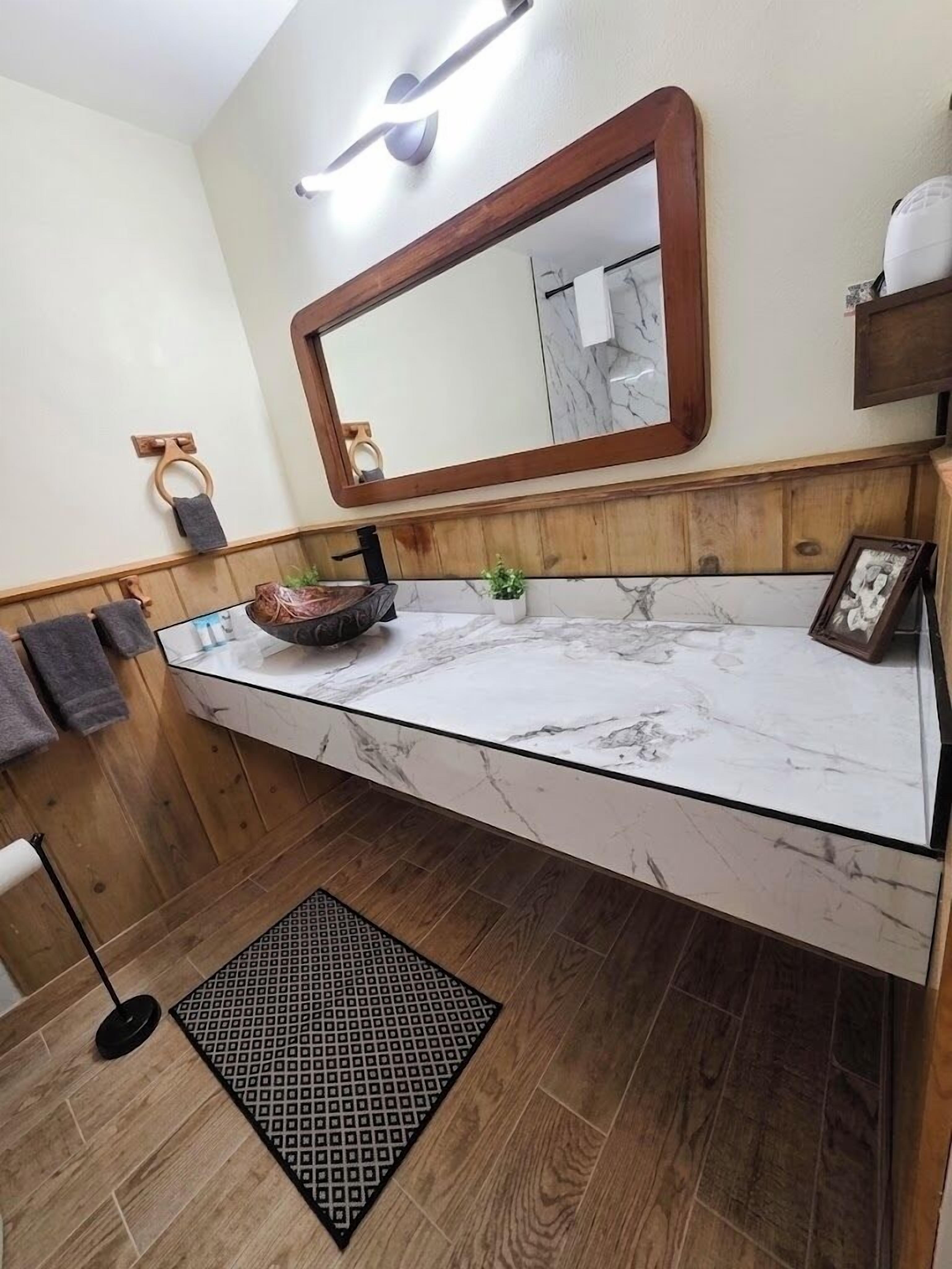 A bathroom with a marble vanity, wooden paneling, a large mirror, and a small potted plant.