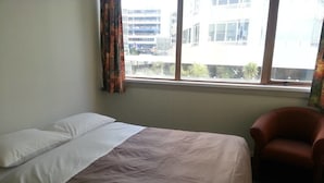 Quarto de hotel com uma cama, uma cadeira e uma janela com vista para edifícios.