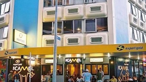 Um edifício com várias lojas, incluindo uma placa visível 'ICAMEL' e uma placa com a inscrição 'ouro exportado'.