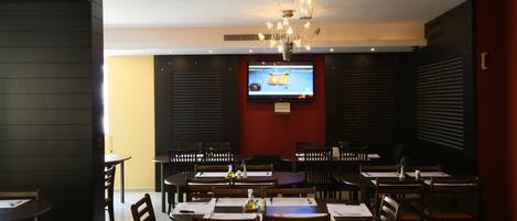 Un restaurante con varias mesas y sillas, un candelabro y una pantalla de televisión al fondo.