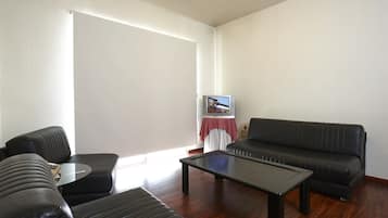 Uma sala de estar com sofá, mesa de centro e televisão sobre um suporte.