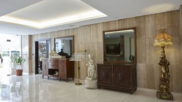 A spacious lobby with a polished tile floor, a wooden reception desk, a large mirror, and a statue.