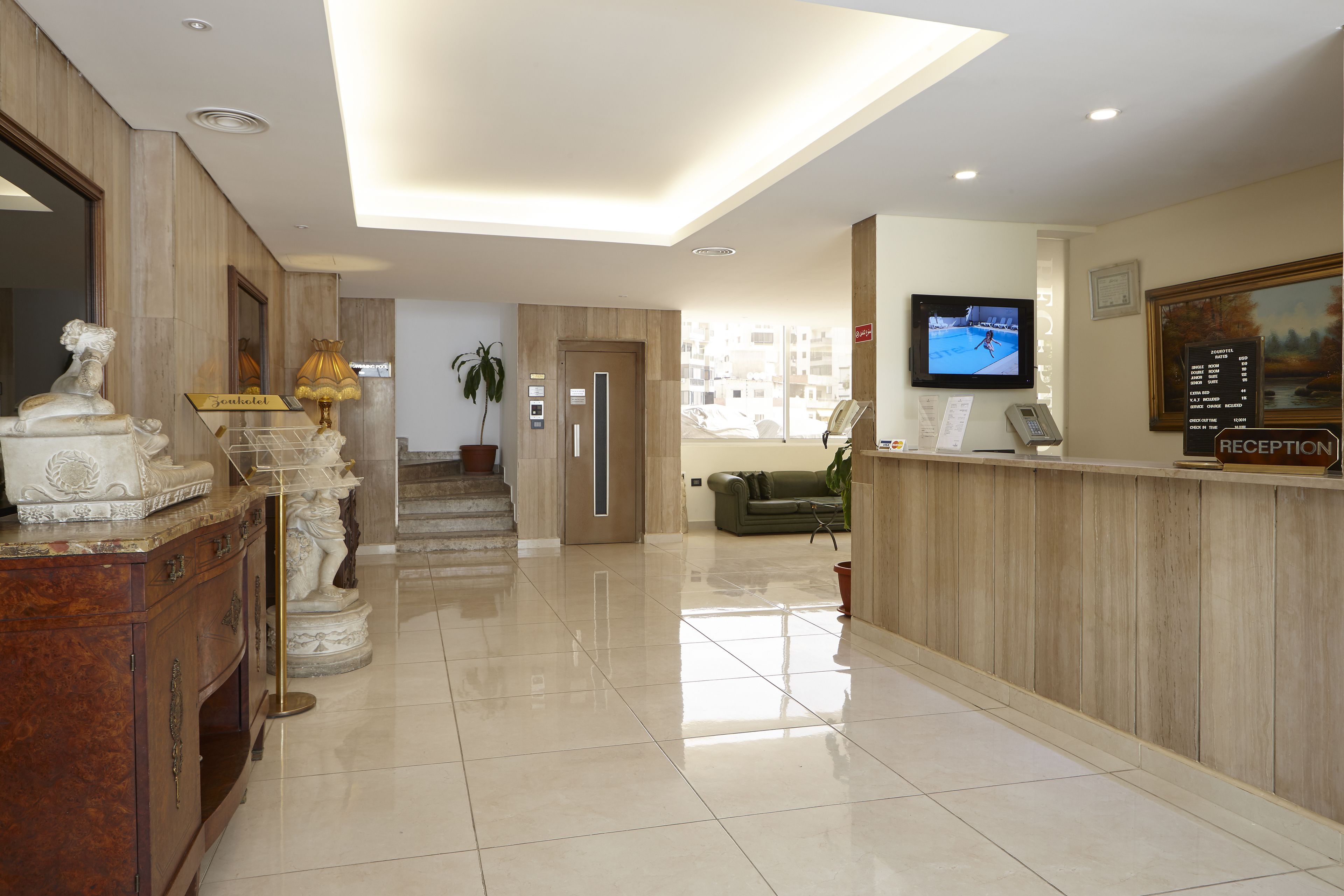 A hotel reception area with a polished floor, a reception desk, a television, and a statue.
