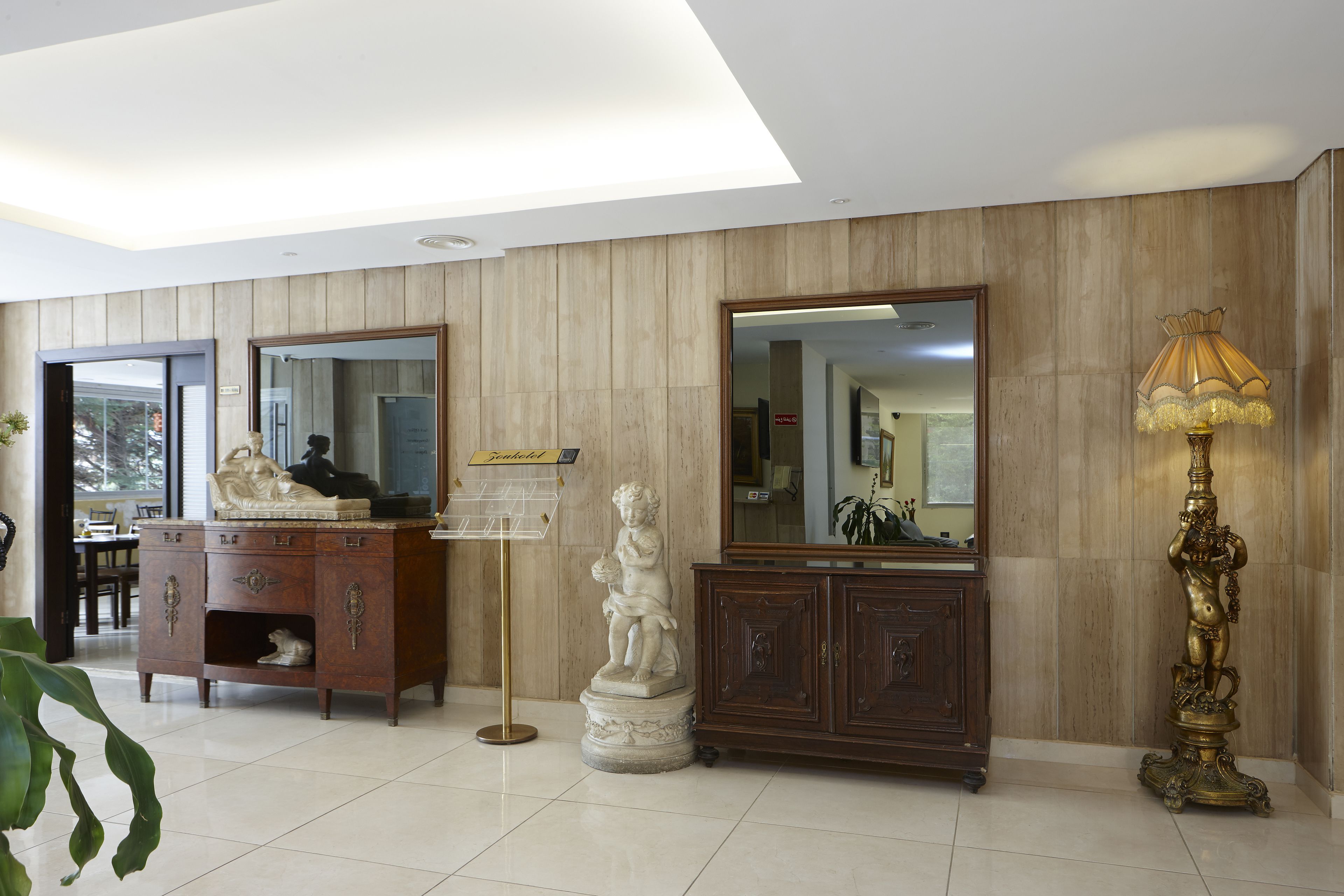 Un vestíbulo amplio con un panel de madera, un espejo grande, una estatua, un aparador y una lámpara de pie.