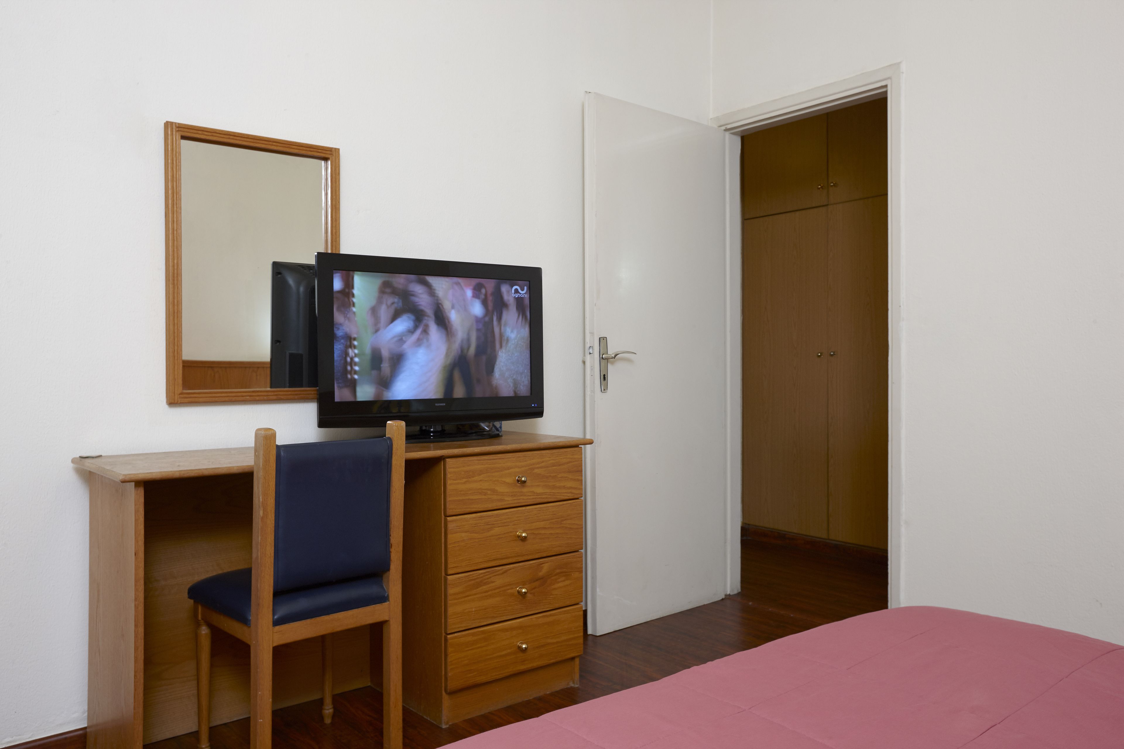 Un dormitorio con un escritorio de madera, una silla, un televisor, un espejo y un armario.