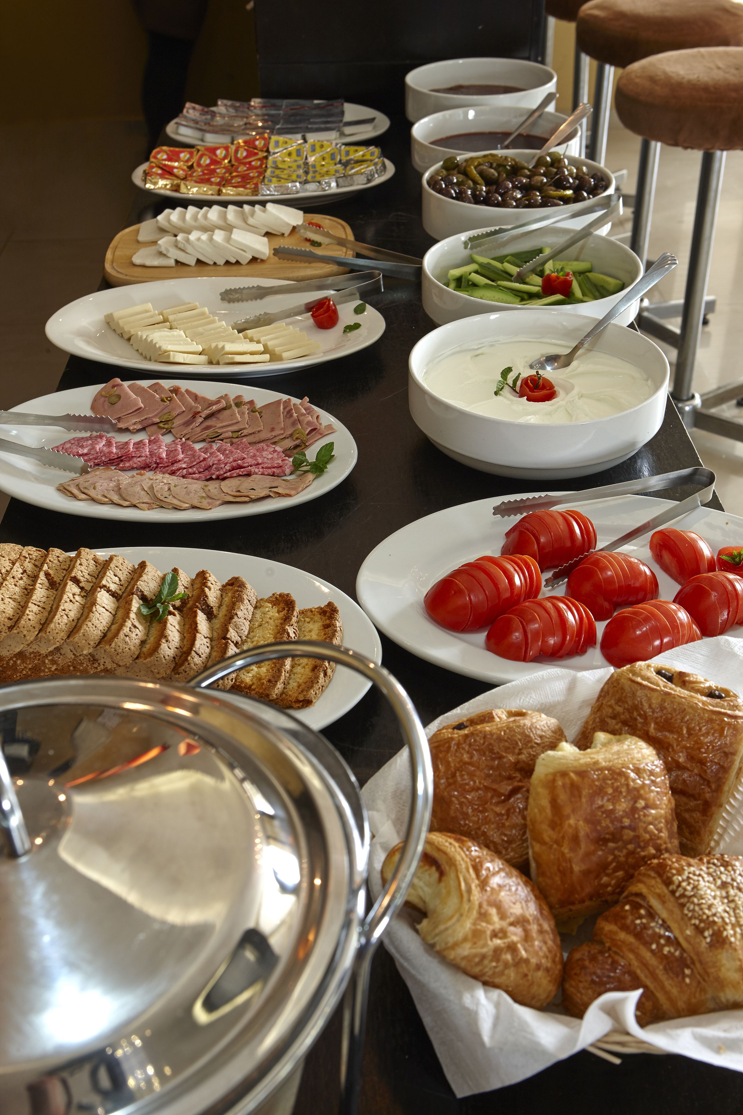Una mesa de buffet con diversos alimentos, incluyendo carnes, quesos y productos de pastelería.