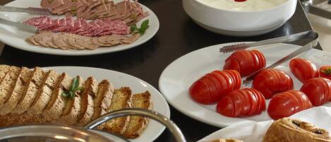 Una mesa de buffet con diversos alimentos, incluyendo carnes, quesos y productos de pastelería.