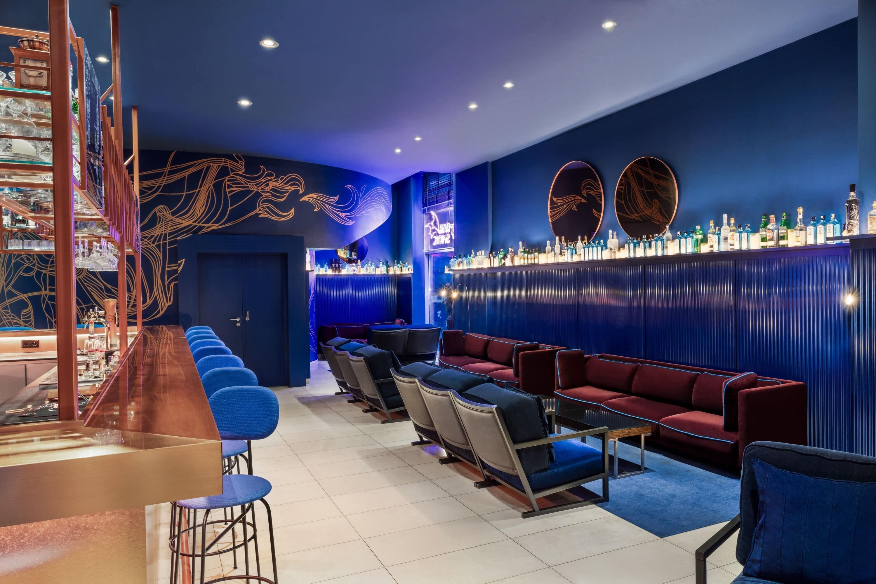 A bar area with a long counter, multiple seating options including bar stools and sofas, and a wall decorated with circular designs.