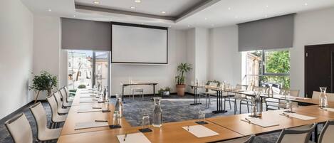 A conference room with a long table, chairs, a projector screen, and potted plants.