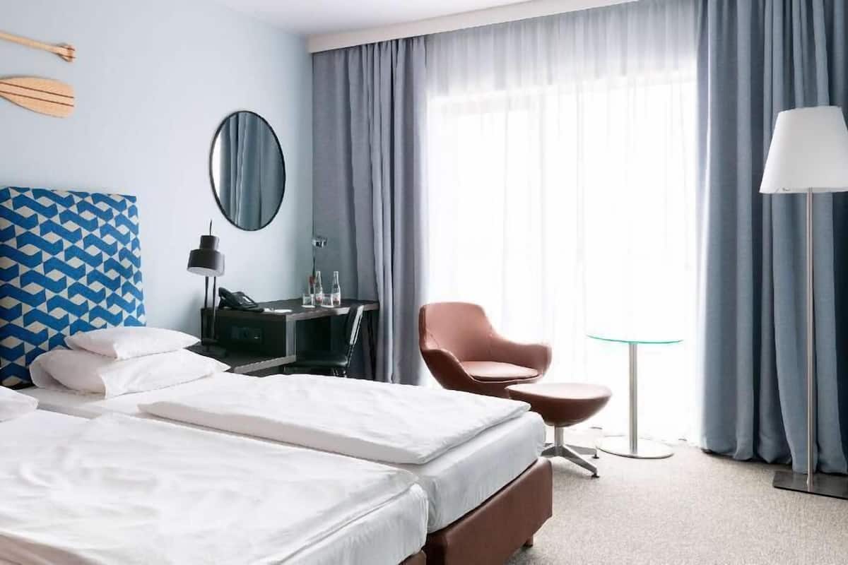 A hotel room with a bed, a desk, a chair, a lamp, and a view of the outdoors.