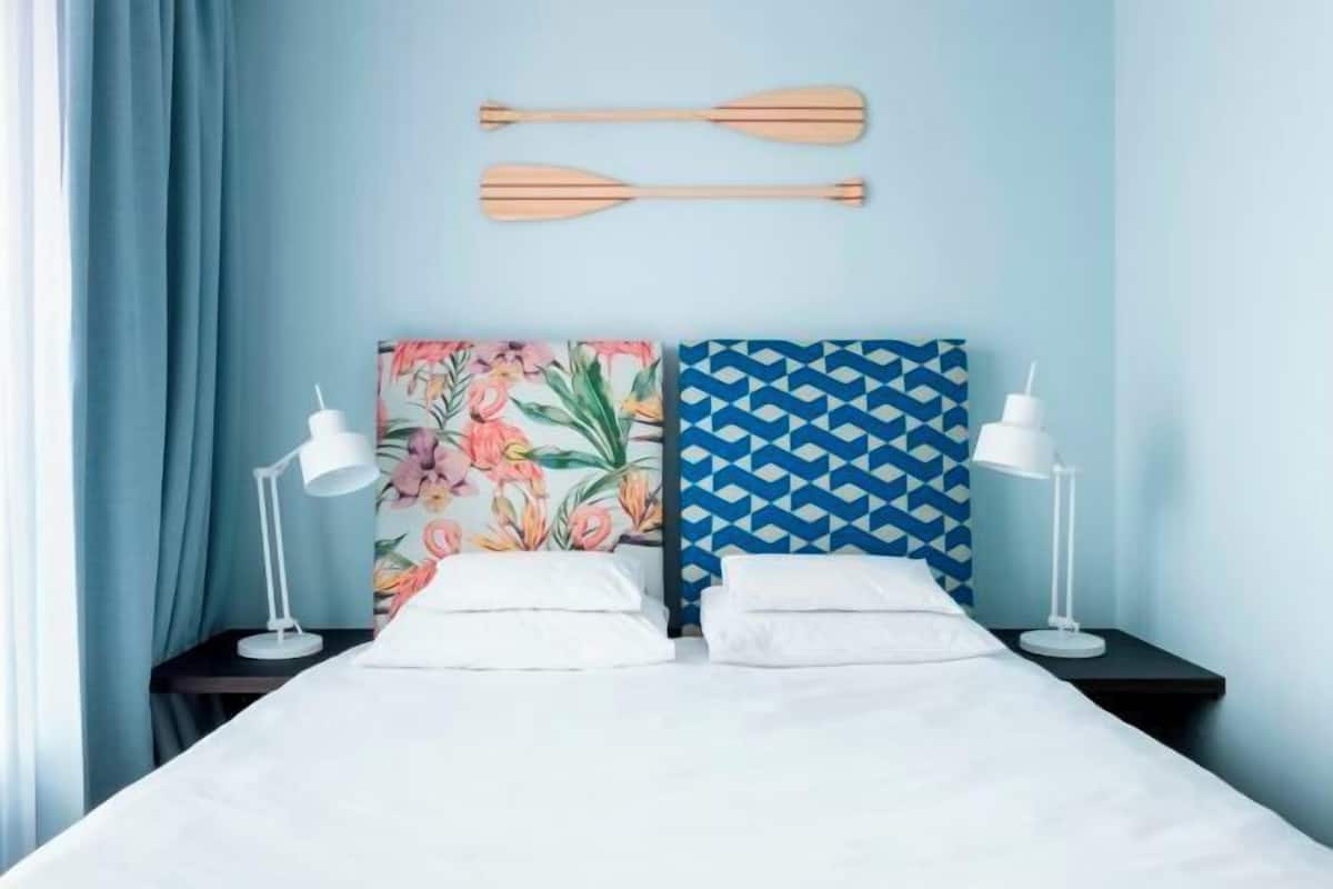 A hotel room with a bed, two nightstands, a pair of wooden paddles on the wall, and two wall art pieces.