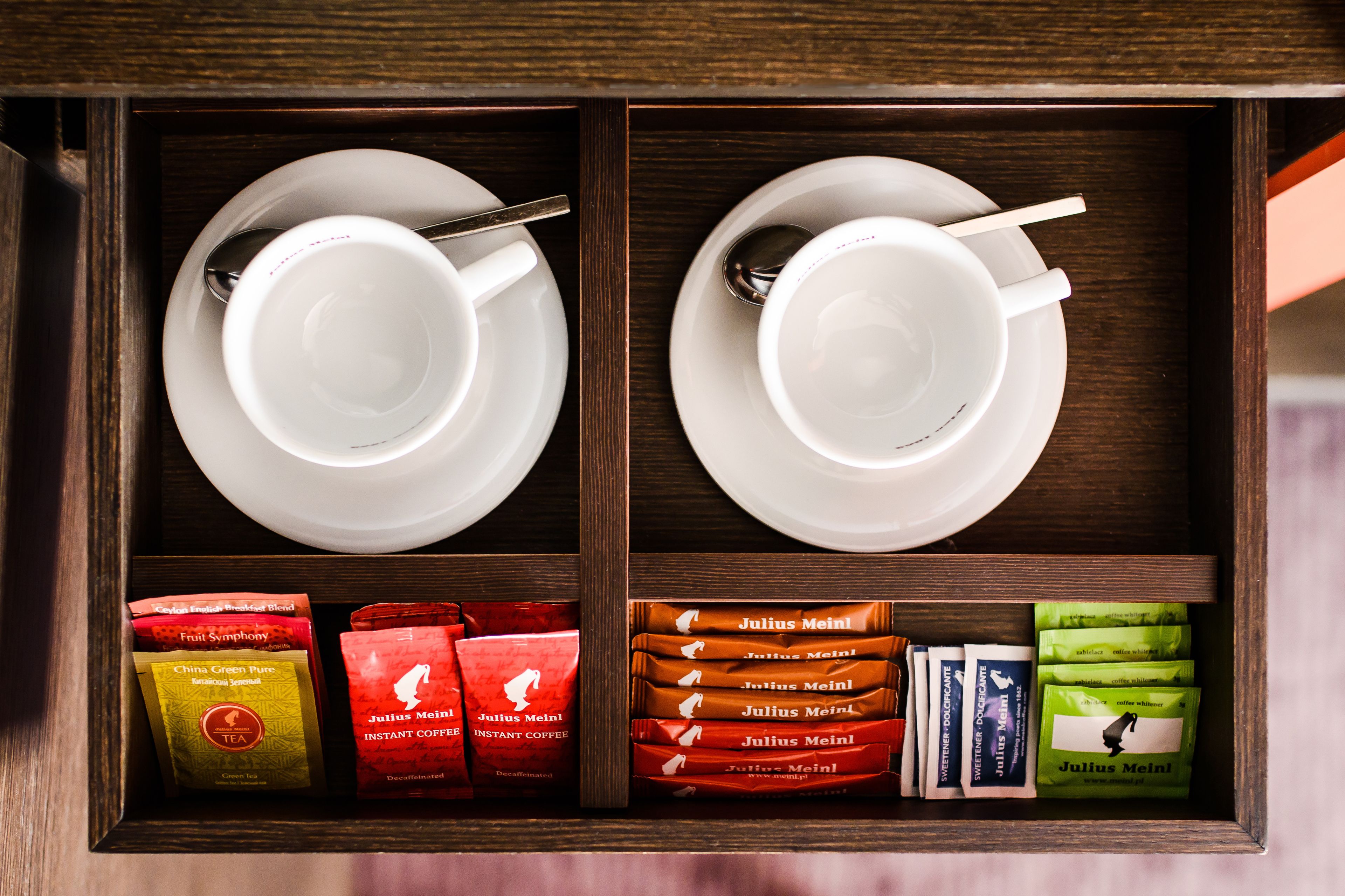 A wooden drawer containing two white cups with spoons, and various instant coffee packets.