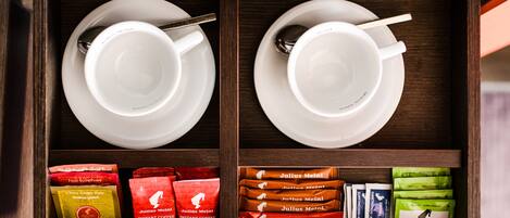 Un cajón de madera con dos tazas blancas y cucharas, además de varios sobres de café instantáneo.