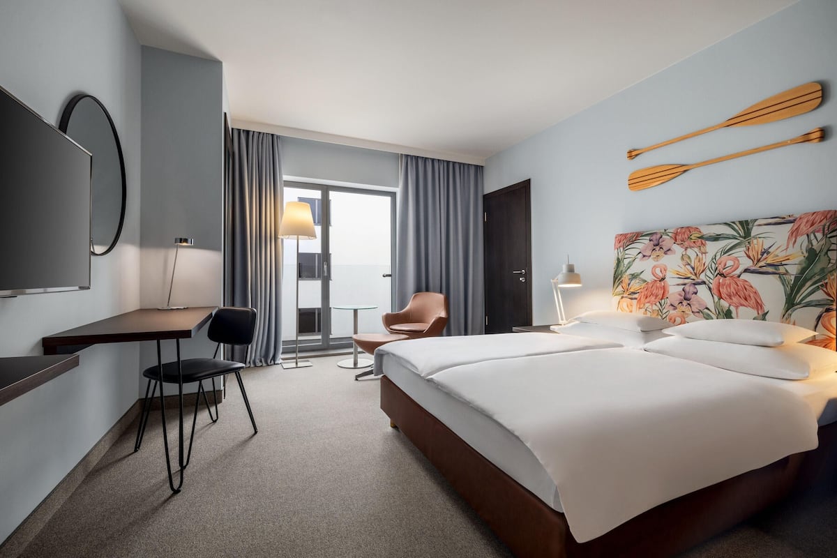 A hotel room with a bed, desk, chair, and a large window with curtains.