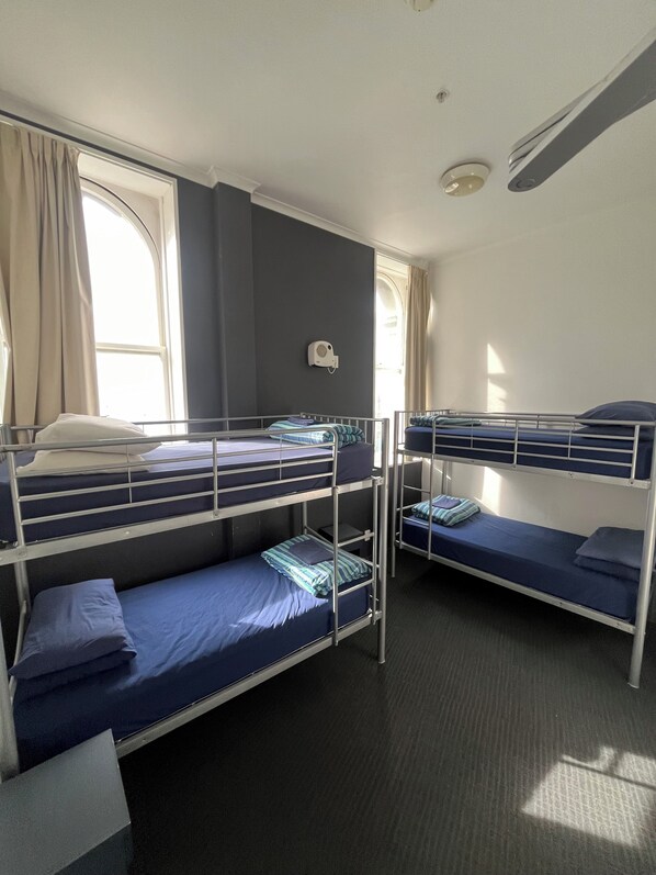 A dormitory room with bunk beds, a window with curtains, and a ceiling fan. - Nomads Capital (Wellington)