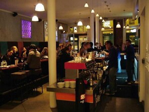 A busy restaurant with tables and chairs, a counter with a cash register, and hanging lights.