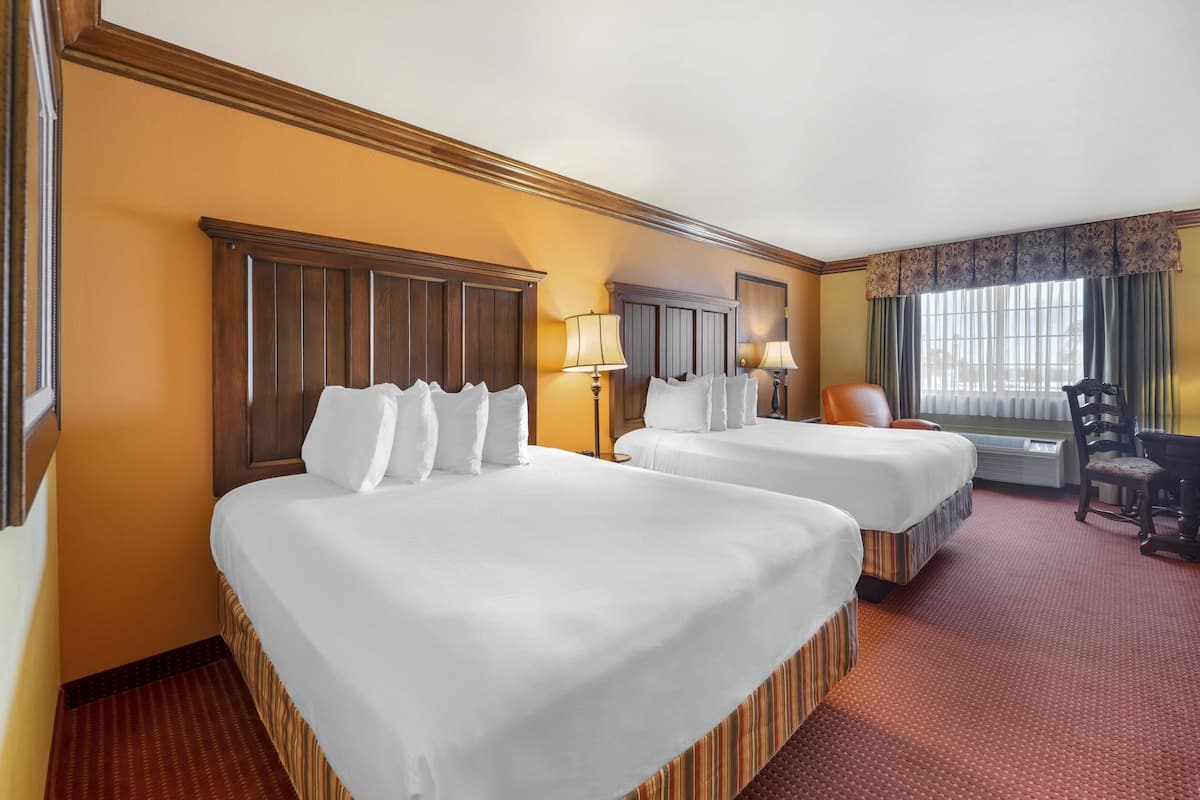 Quarto de hotel com duas camas, uma mesa, uma cadeira e uma janela com cortinas.