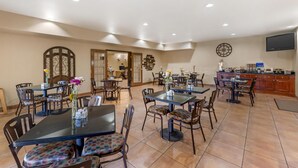 A spacious dining area with multiple tables and chairs, a kitchen area with a flat-screen TV, and a decorative wall clock. - Best Western San Isidro Inn (Laredo)