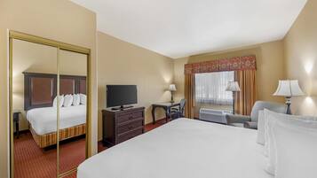 Een hotelkamer met een groot bed, een televisie, een bureau, twee stoelen, een spiegel en een raam met gordijnen.