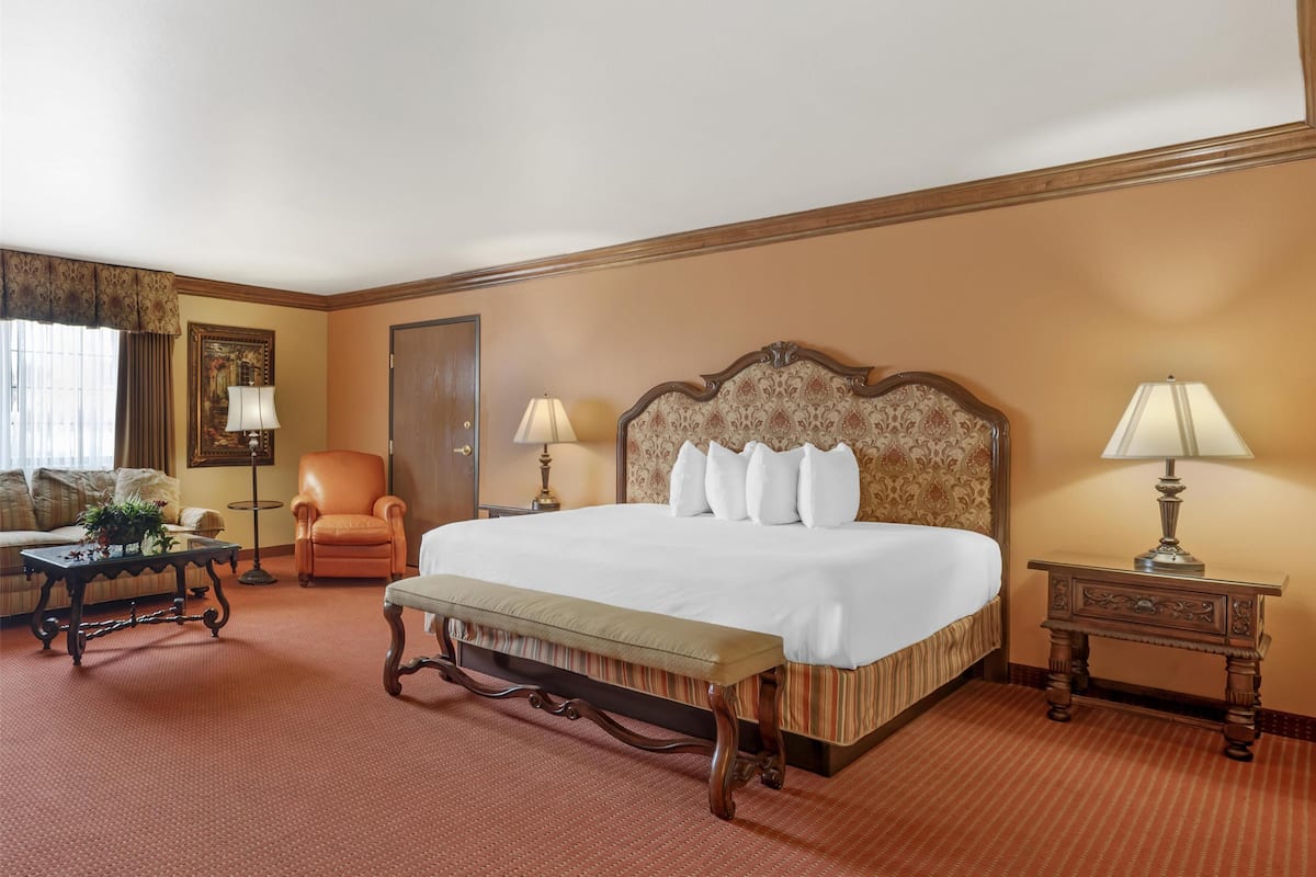 Quarto de hotel com uma cama grande, uma cadeira, uma mesa e um abajur.