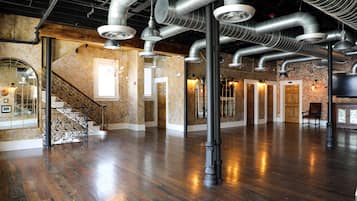 A spacious room with polished wooden floors, exposed ductwork, and a staircase with ornate railings.