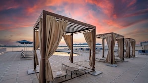 Outdoor seating areas with tables and chairs, connected by a pergola structure, overlooking a body of water and a bridge. - Hilton Baton Rouge Capitol Center (Baton Rouge)