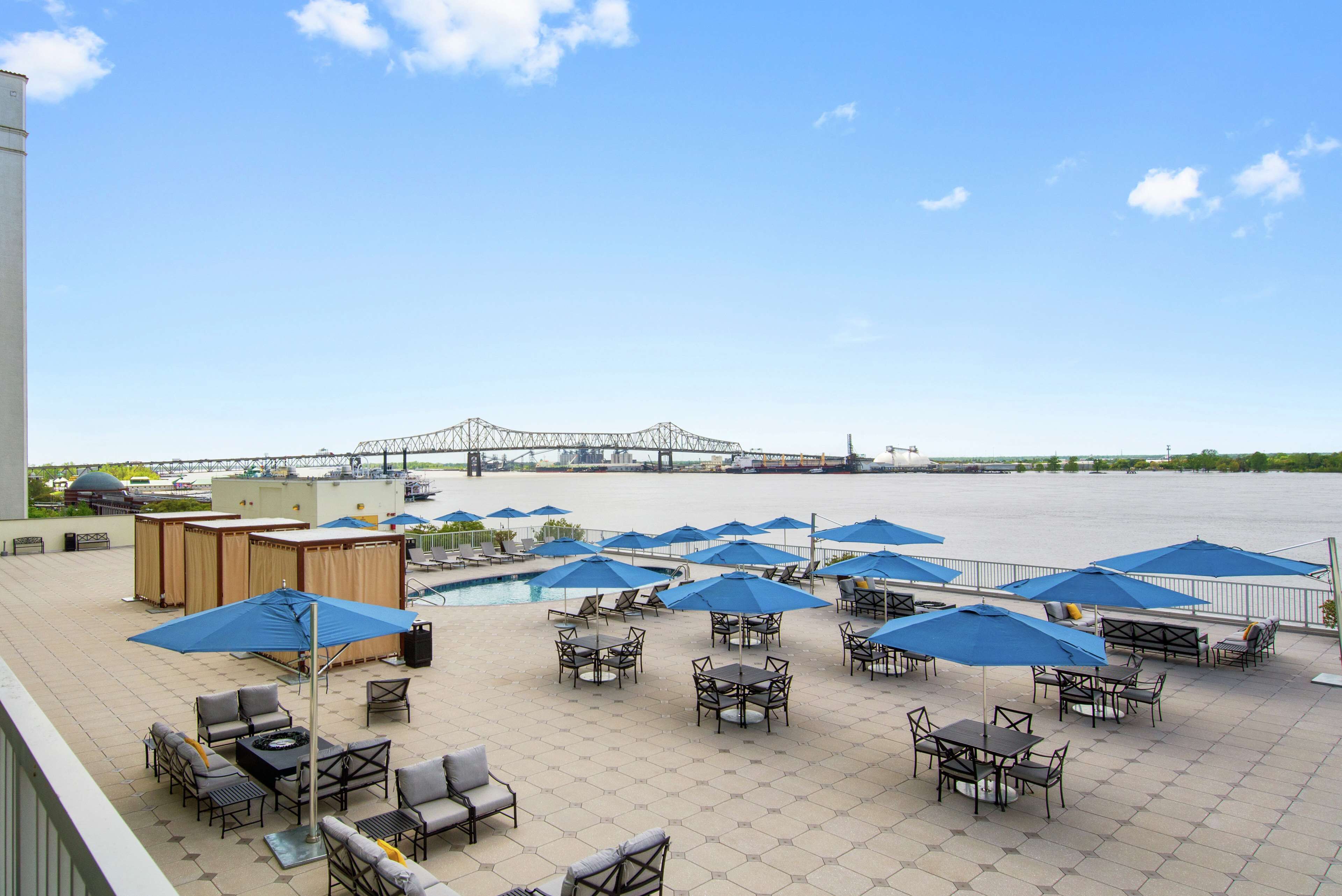 A rooftop patio with outdoor seating, umbrellas, and a view of a bridge.