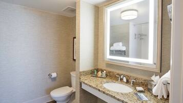 A modern bathroom with a granite countertop, two sinks, a large mirror, and a toilet.