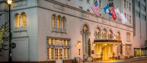 Un hotel histórico con ventanales de arco, una entrada imponente y varias banderas.
