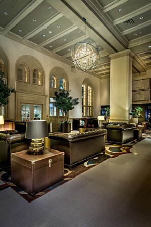 A spacious lobby with leather sofas, a large chandelier, and a grand staircase.
