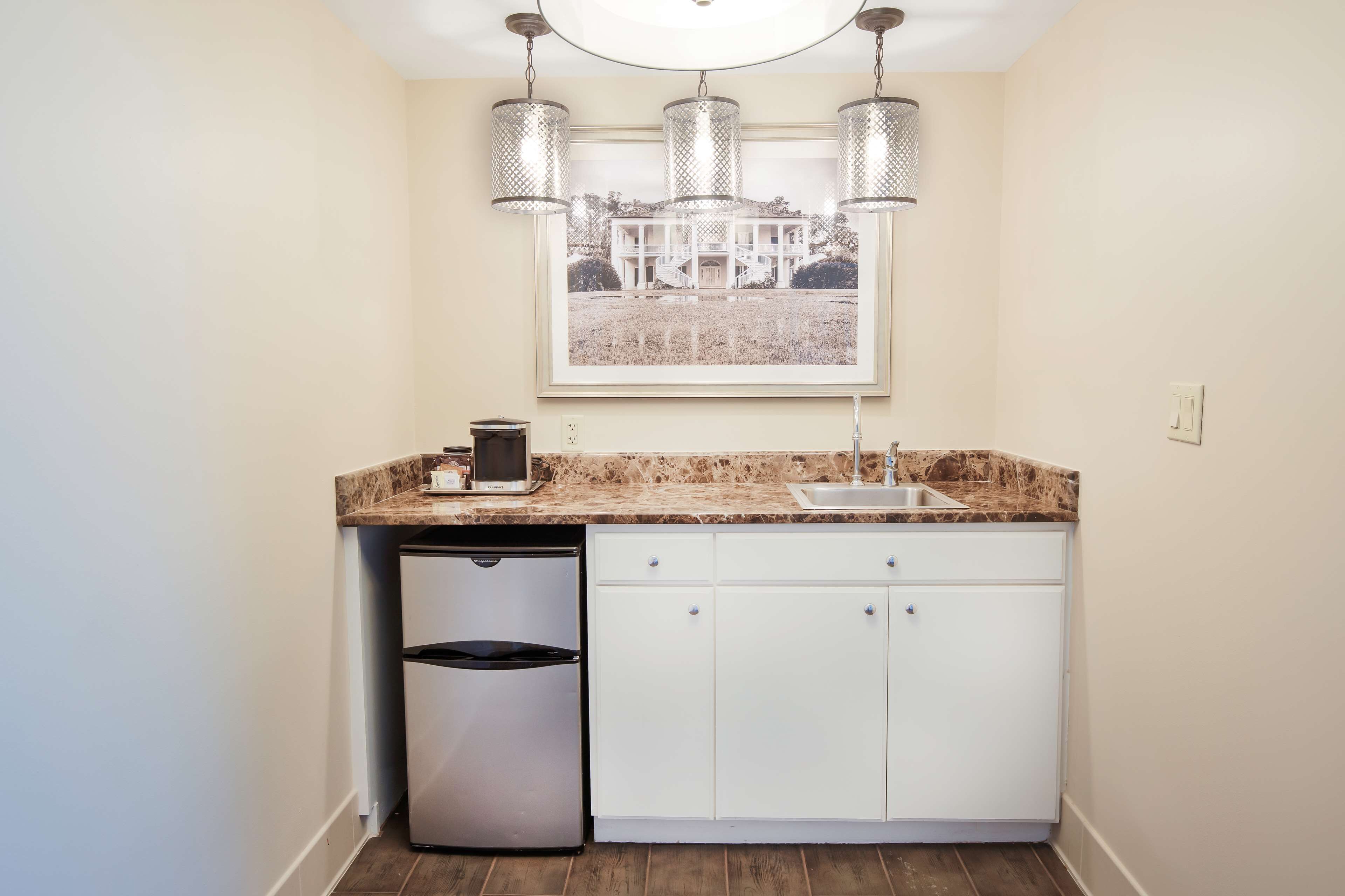 A kitchen with a built-in dishwasher, white cabinets, a marble countertop, and a framed picture above the sink.