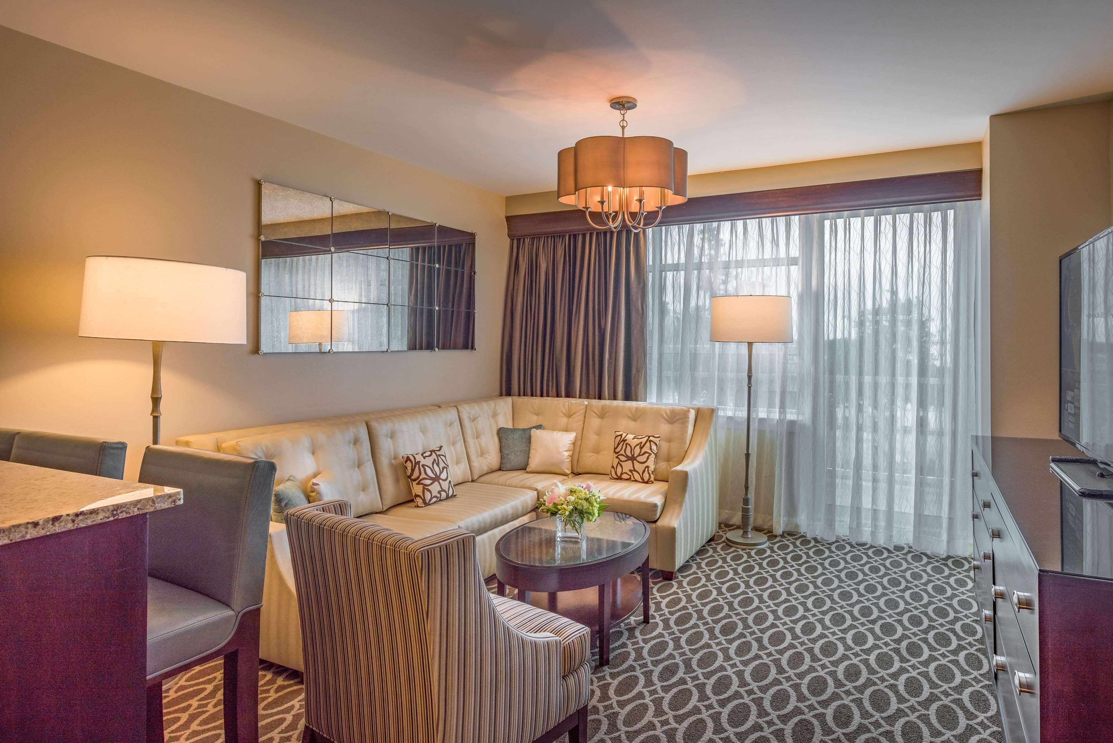 Een hotelkamer met een bank, fauteuils, een tafeltje, een televisie en een groot raam met gordijnen.