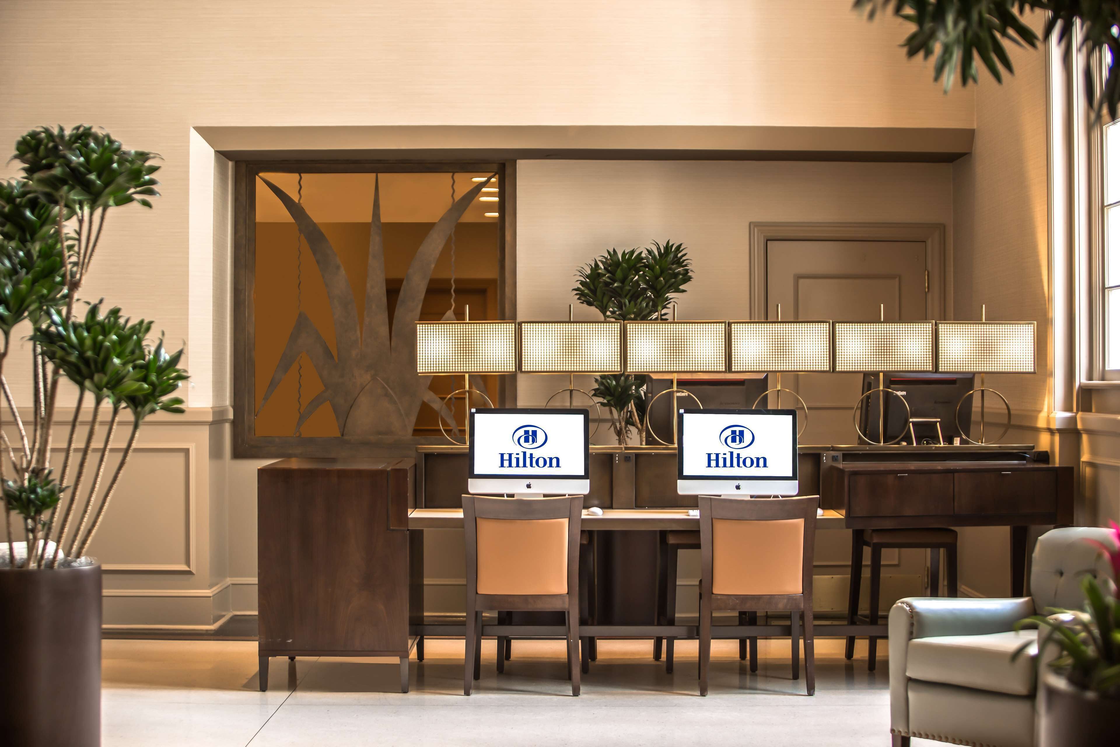 Eine Hotteillobby mit zwei Computermonitoren, die das Hilton-Logo zeigen, einem Empfangsbereich und einem Klavier.
